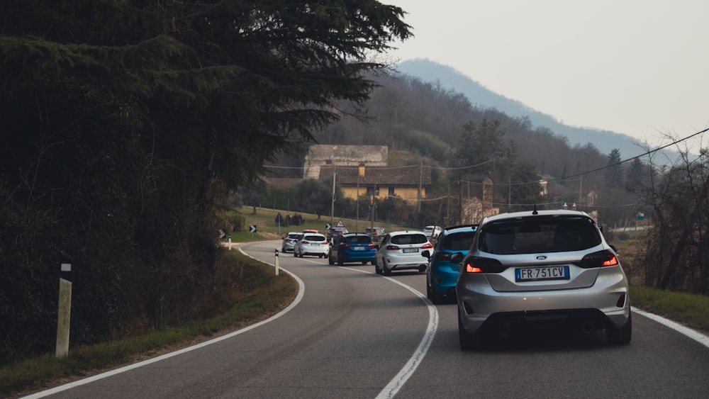 a group of cars driving down a road next to a forest