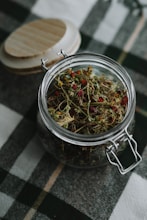 a glass jar filled with dried herbs on a checkered table cloth
