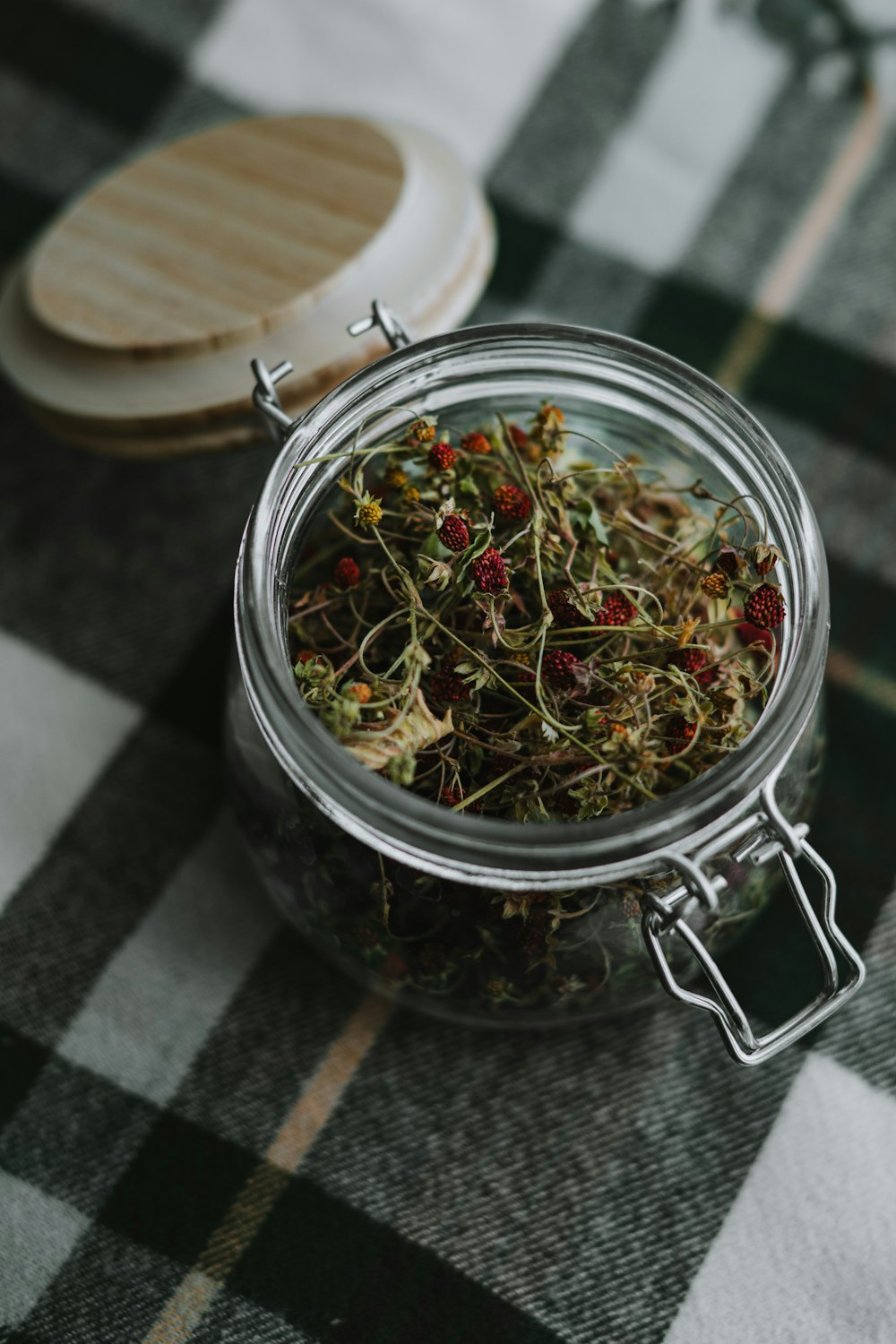 a glass jar filled with dried herbs on a checkered table cloth