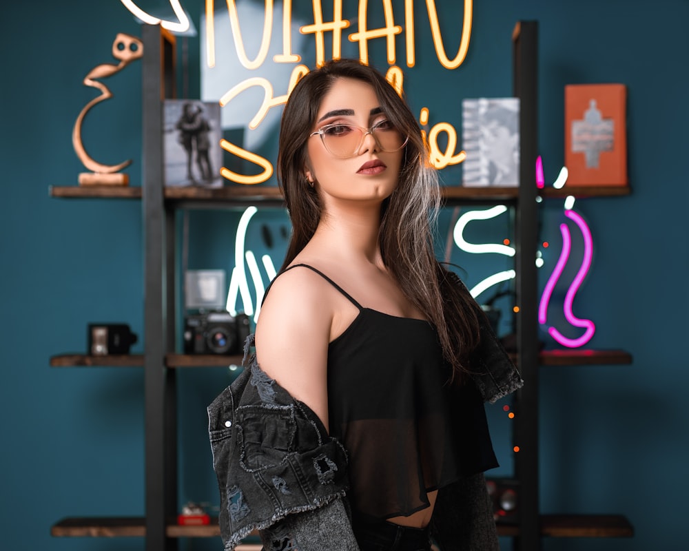 a woman in a black top is standing in front of a neon sign