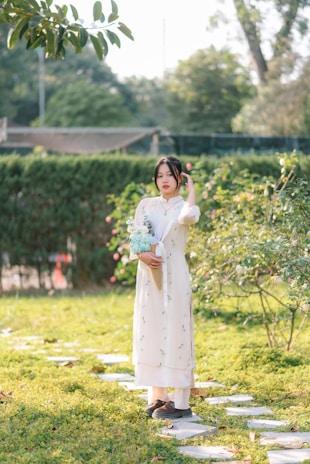 Softly lit photo of a woman in a flowing peach dress holding a bouquet of wildflowers in a sunlit garden.