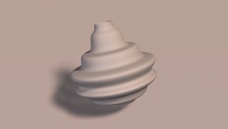 A smooth, sculptural object with a spiral or layered design, resembling a modern art piece or a decorative vase, is placed against a neutral background. The object appears to be made of a material like ceramic or metal.