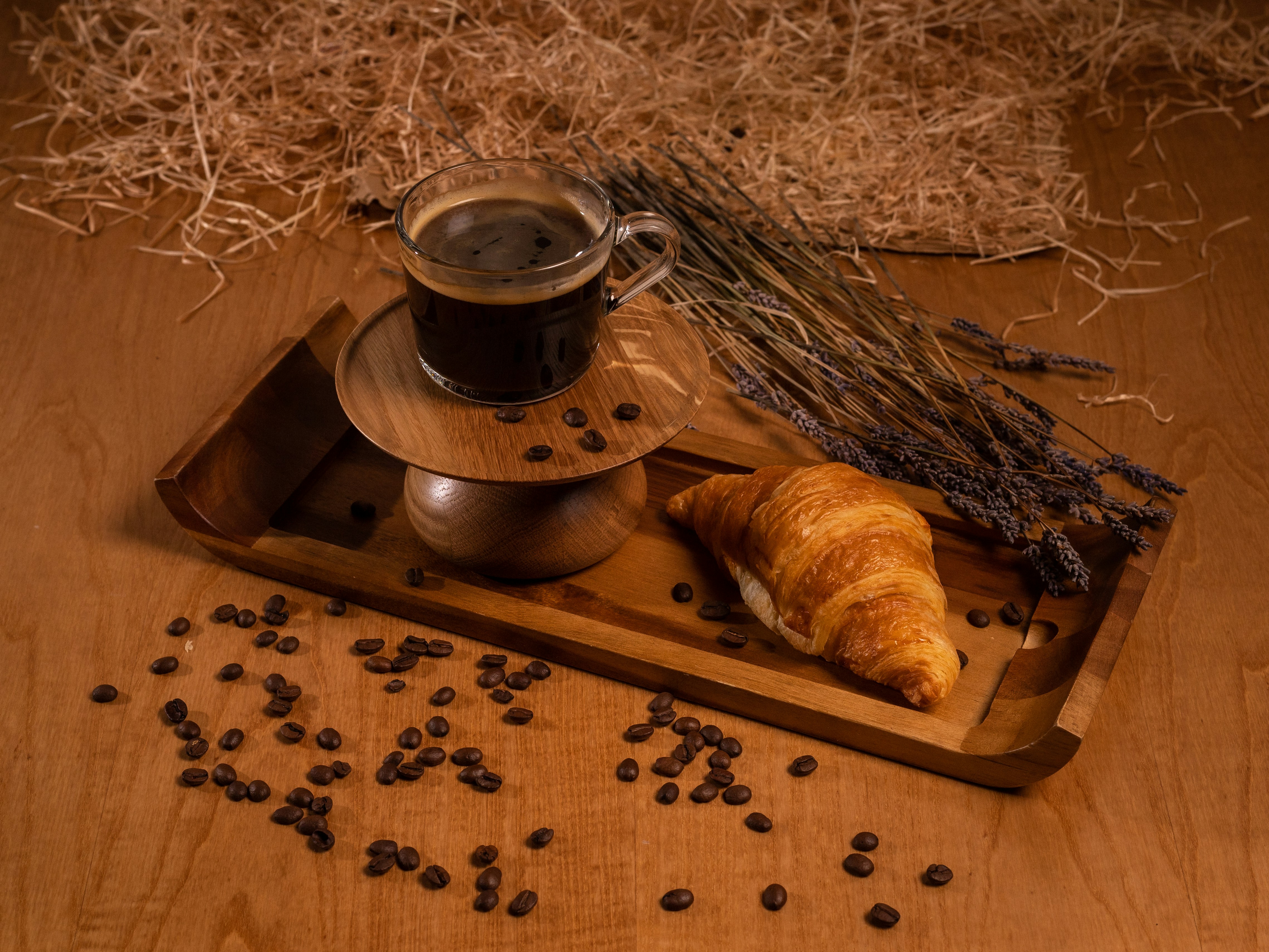 a wooden tray topped with a cup of coffee and a croissant