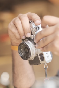 Hands are adjusting the settings on a vintage-style camera with a large lens. The camera has a black and silver body, and the setting is warmly lit with a soft focus background.