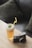 A refreshing iced tea garnished with mint leaves and a yellow straw is placed on a wooden table beside a vintage-style camera. The background features dark, soft cushions suggesting a cozy setting.
