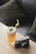 A refreshing iced tea garnished with mint leaves and a yellow straw is placed on a wooden table beside a vintage-style camera. The background features dark, soft cushions suggesting a cozy setting.