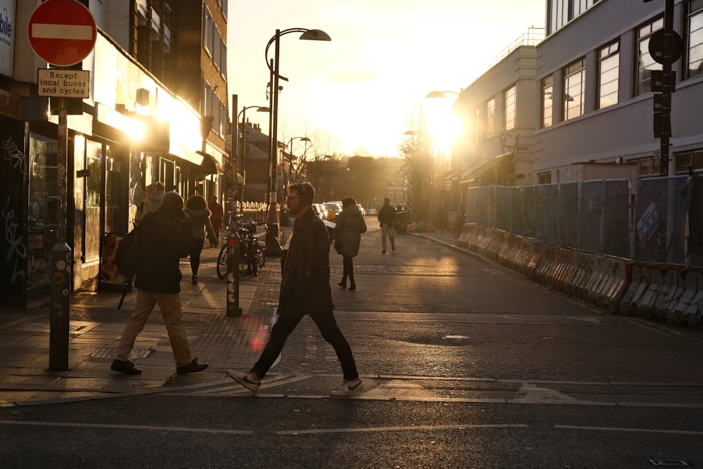 a group of people crossing a street at sunset