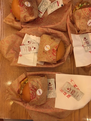 Stacked burgers with fresh lettuce and tomato, wrapped in omg feast branded paper on a clean white table.