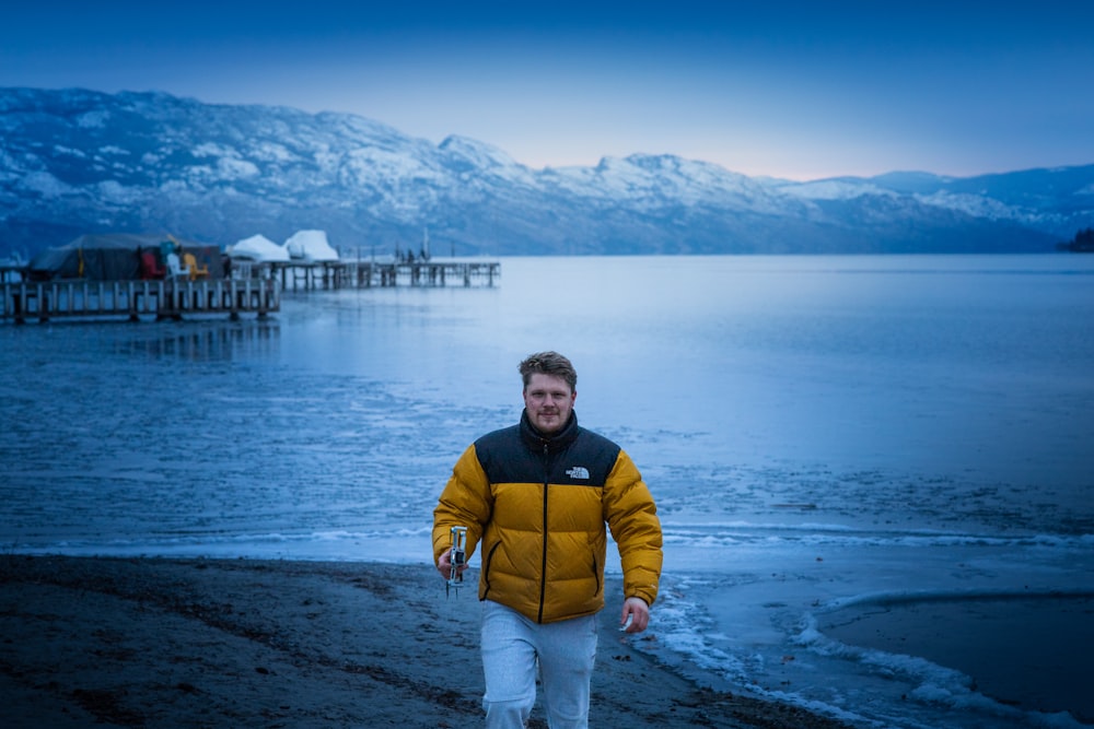 a man in a yellow jacket walking on a beach