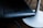 A close-up view of a dark leather chair seat beside a white, round table base. The chair has a smooth, cushioned surface with visible stitching. The table base is sleek and has a modern design. The background suggests a wooden floor.