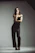 A confident woman smiling, dressed in elegant neutral tones, standing in a modern minimalist room.