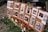 A display board is set up with several images and QR codes, each photo depicting scenes of destruction and aid efforts. Red carnations are pinned next to some of the images, and more flowers are laid at the base of the board.