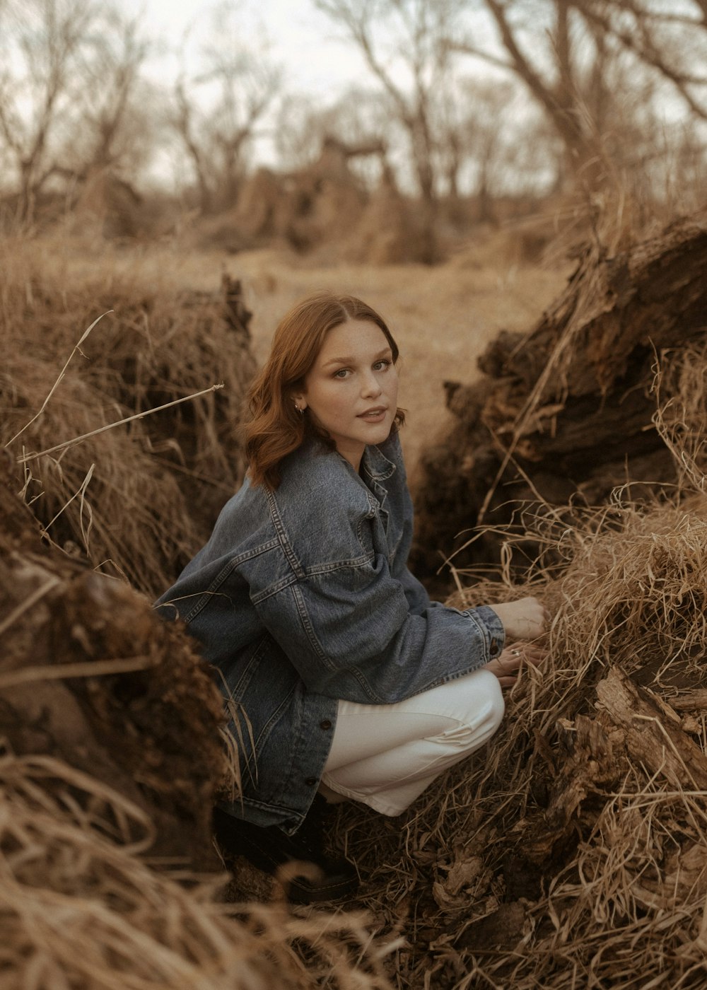 a woman kneeling down in a field of dry grass