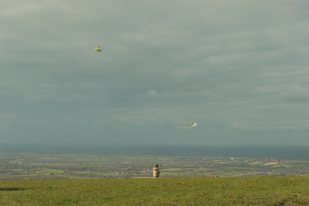 a person standing on top of a grass covered hill flying a kite