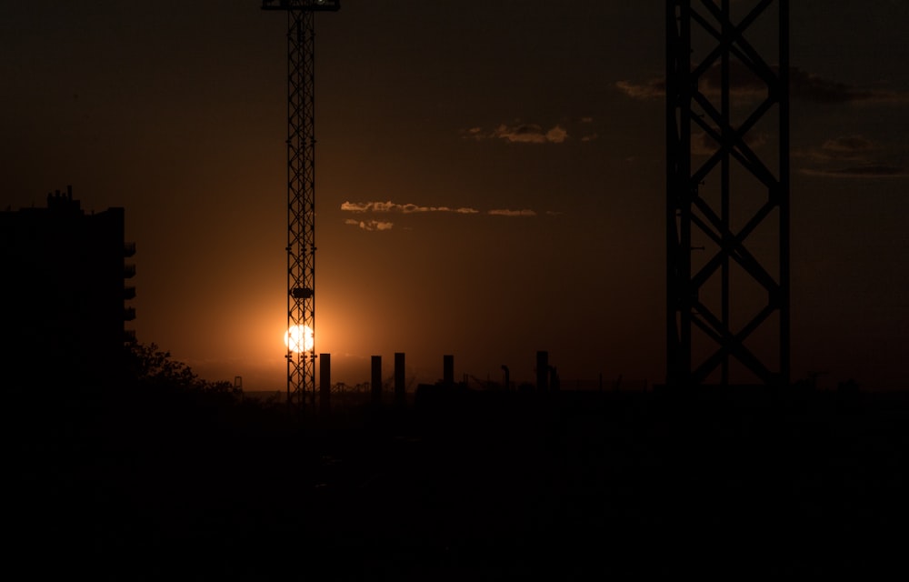 the sun is setting behind a tower crane