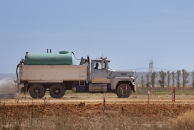 a truck driving down a dirt road next to a field