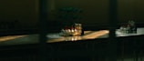 A dimly lit laboratory table with an arrangement of test tubes, some filled with liquid in varied colors. There is also a molecular model in the background. Sunlight through the window casts dramatic shadows and highlights on the surface.