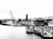 A bustling industrial port area with several ships docked along the water. Cranes tower over the ships, loading or unloading cargo. In the background, a dense urban skyline with numerous high-rise buildings provides a stark contrast to the busy port activity.