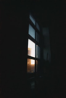 A softly lit, moody black-and-grey corner of a room with shadows stretching across a silver-lined window.