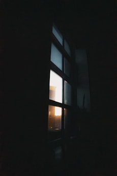 A softly lit, moody black-and-grey corner of a room with shadows stretching across a silver-lined window.