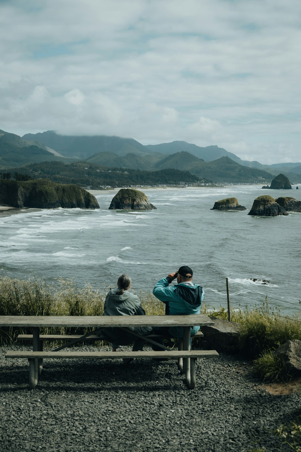 two people sitting on a bench looking out at the ocean