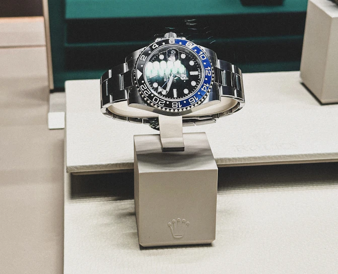 A sleek luxury watch with a golden bezel resting on a deep black velvet cushion