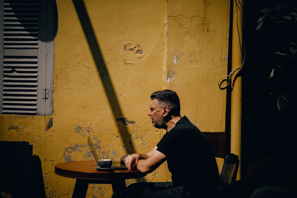 Un homme assis à une table devant un mur jaune