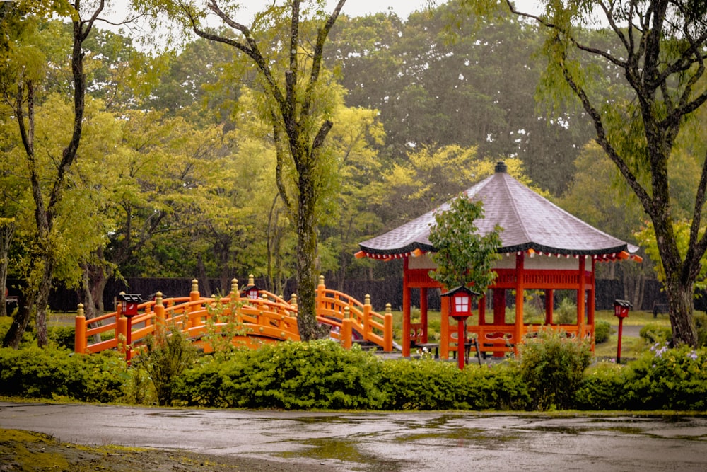 a red and white gazebo in a park surrounded by trees