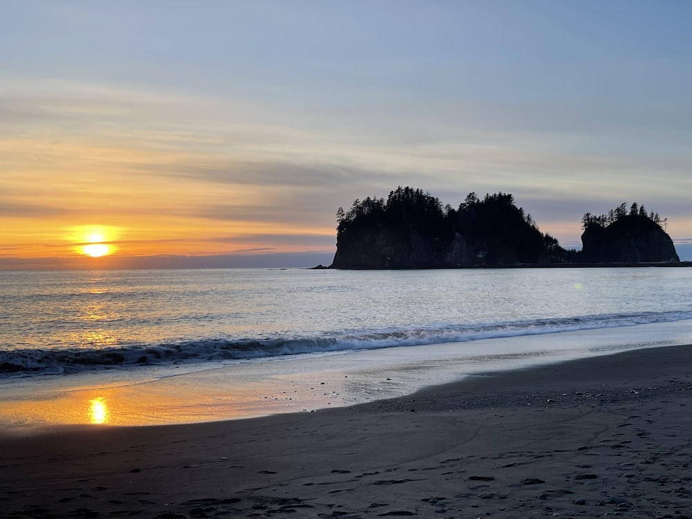 the sun is setting on a beach with two small islands in the distance