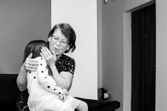 A young caregiver warmly assisting a smiling senior woman at home.