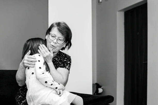 A young caregiver warmly assisting a smiling senior woman at home.