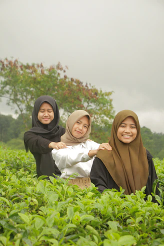 three women in hijabs are sitting in a field