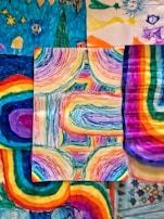 A collection of vibrant, multicolored drawings featuring abstract patterns and shapes. The central piece showcases dynamic, curved lines with a rainbow spectrum, surrounded by other artworks with similar vivid hues and whimsical designs.