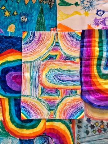 A collection of vibrant, multicolored drawings featuring abstract patterns and shapes. The central piece showcases dynamic, curved lines with a rainbow spectrum, surrounded by other artworks with similar vivid hues and whimsical designs.
