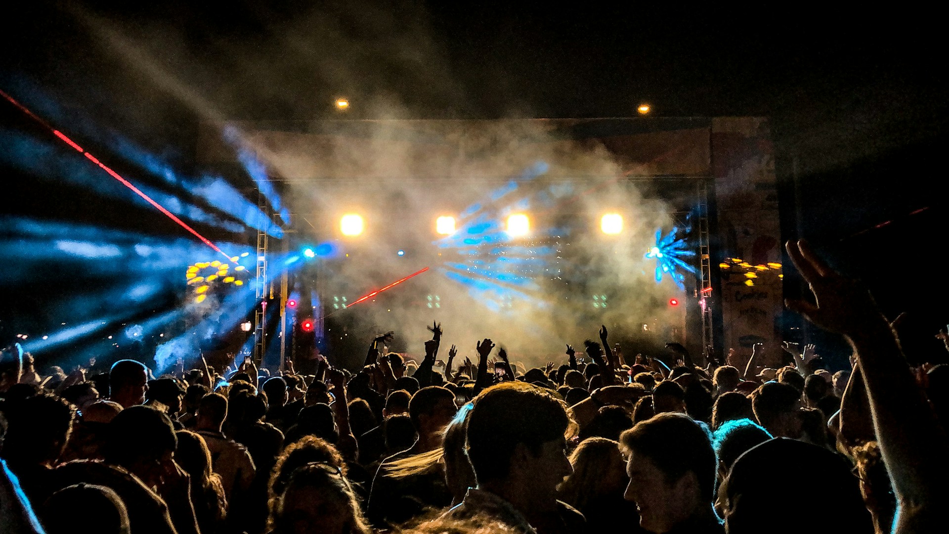 An energetic crowd enjoying a live concert under the stars, with bright lights illuminating the stage.