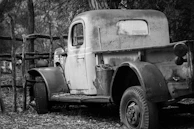 A classic rusted pickup truck parked beside a weather-beaten fence in a rural setting.