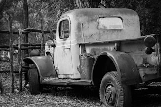 A classic rusted pickup truck parked beside a weather-beaten fence in a rural setting.