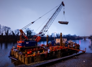 Launching gantry lifting heavy bridge segments over a river at sunrise