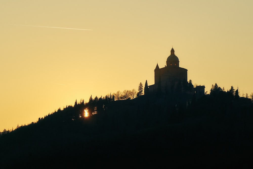 a church on a hill with the sun setting behind it