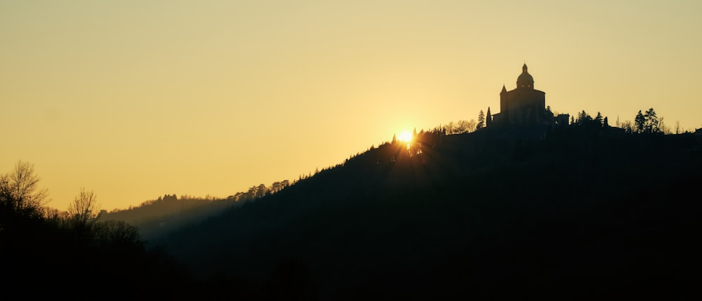 a church on a hill with the sun setting in the background