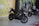 A sleek black Kawasaki motorcycle is prominently displayed indoors. The showroom features a bright yellow wall with the logo 'GM MOTO' repeated across it. In the background, another motorcycle can be observed along with a printed outdoor scene, suggesting an adventurous theme.