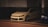A white modified car with large wheels is parked in a dimly lit garage next to other vehicles. The car has a sleek design with a lowered body, and the setting is predominantly dark with artificial lighting highlighting the car's features.