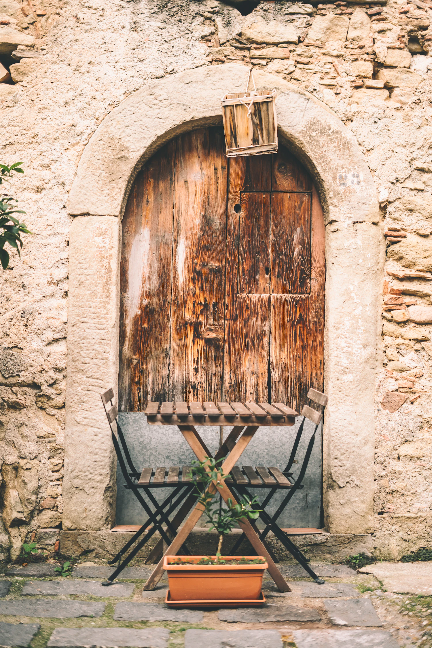 An arched weathered wooden door set in stone with a folding table beside it