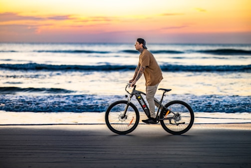 Cyclist riding along a scenic beach trail at sunset with a vibrant sky.