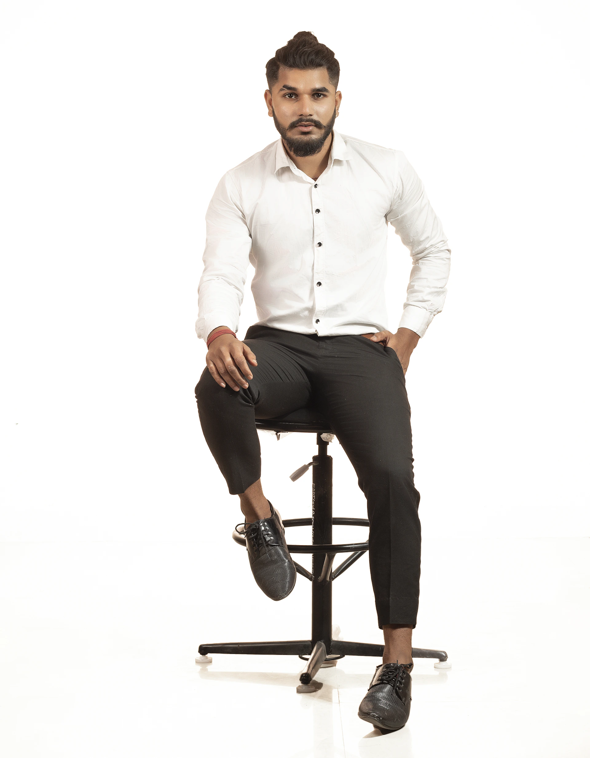A confident man with a sharp haircut and well-groomed beard sitting in a stylish, dark premium barbershop illuminated by subtle golden lights.
