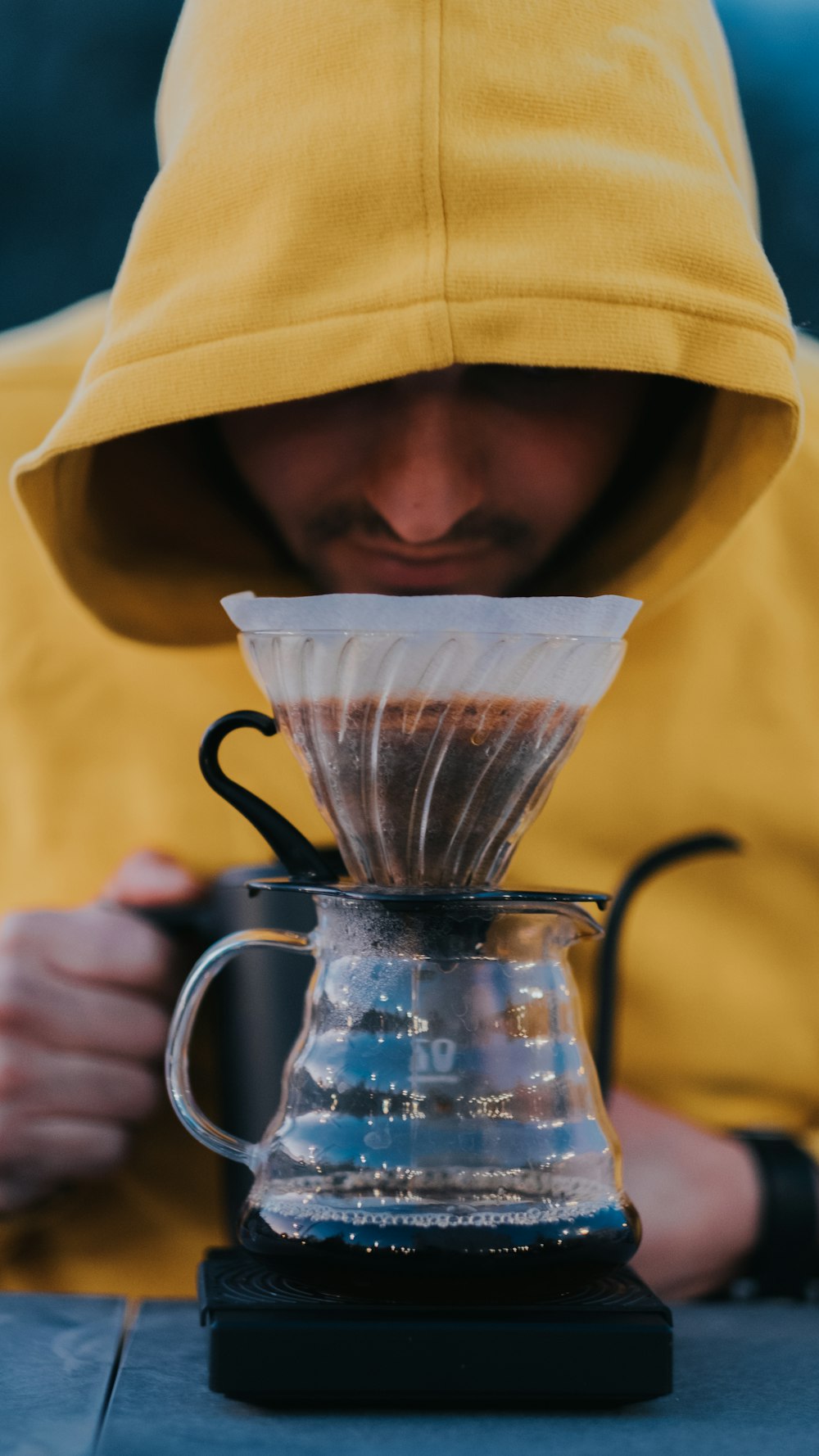 a man in a yellow hoodie pouring coffee into a coffee pot