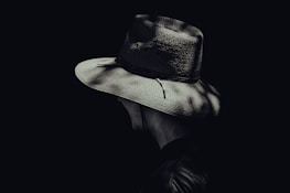 A silhouette of a detective with a hat and trench coat, pondering over clues.