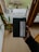 A person's hand is holding a black package with a label that reads 'LOT61'. The background features a wooden deck with some plant pots and a green lawn visible outside a glass door. The setting seems to be inside a cozy room with wooden floors and furniture.