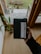 A person's hand is holding a black package with a label that reads 'LOT61'. The background features a wooden deck with some plant pots and a green lawn visible outside a glass door. The setting seems to be inside a cozy room with wooden floors and furniture.