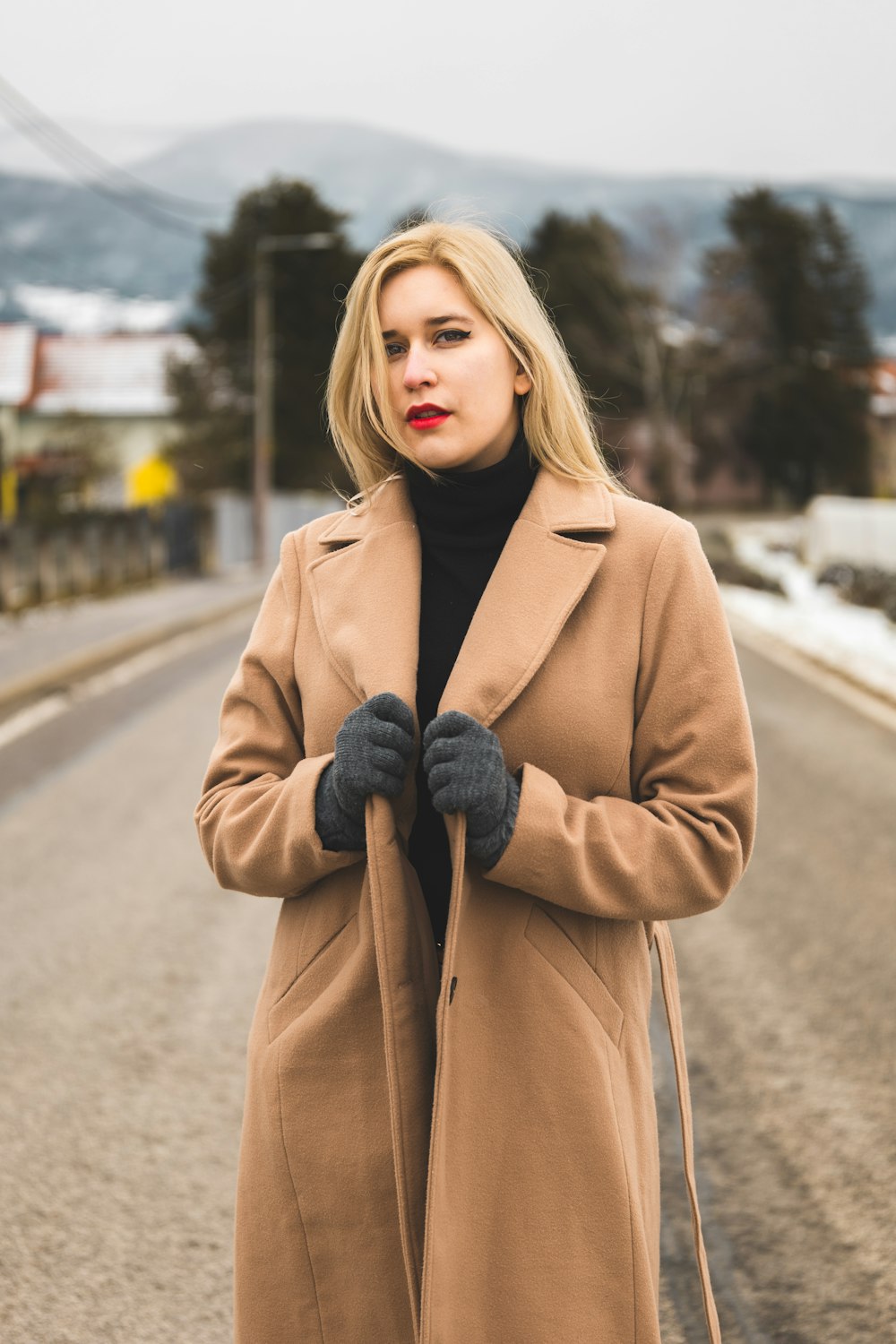 a woman standing on a road wearing a coat and gloves